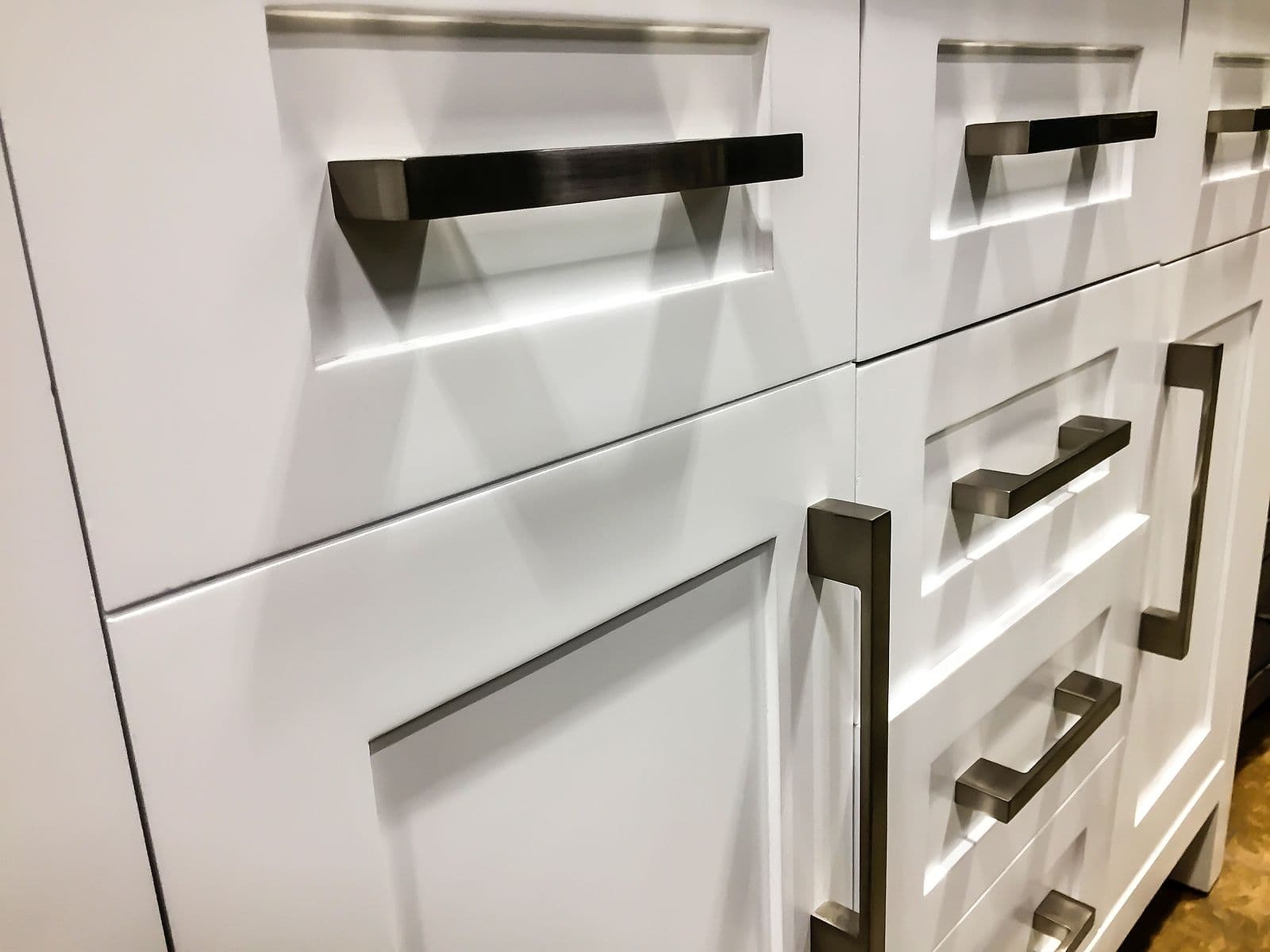 Modern kitchen cabinet display with white drawers and doors, chrome handles, and integrated LED lighting in recessed shelves