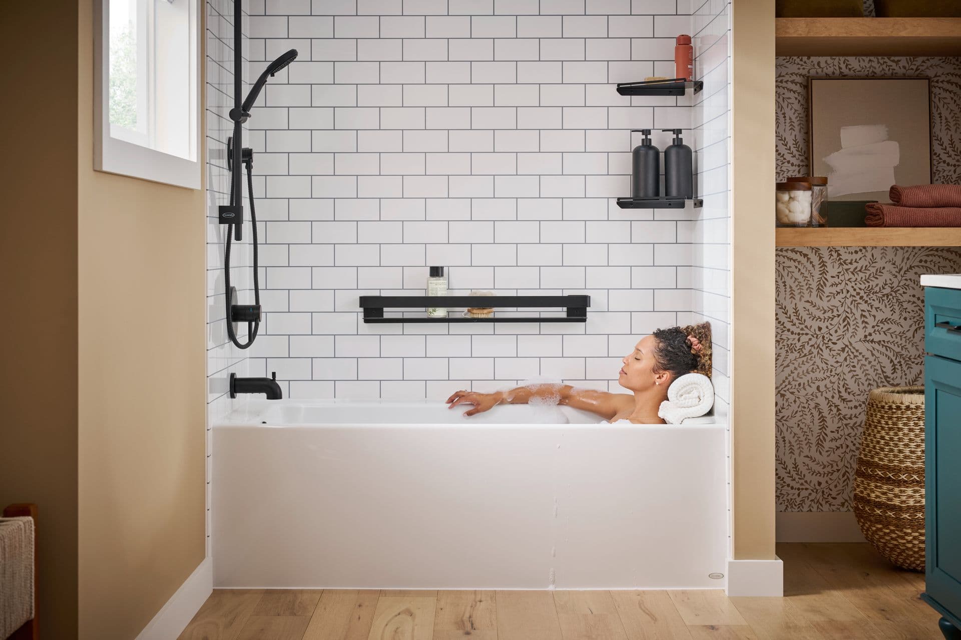 Woman relaxing in a modern bathtub with white subway tile walls, black fixtures, and organized bathroom shelving