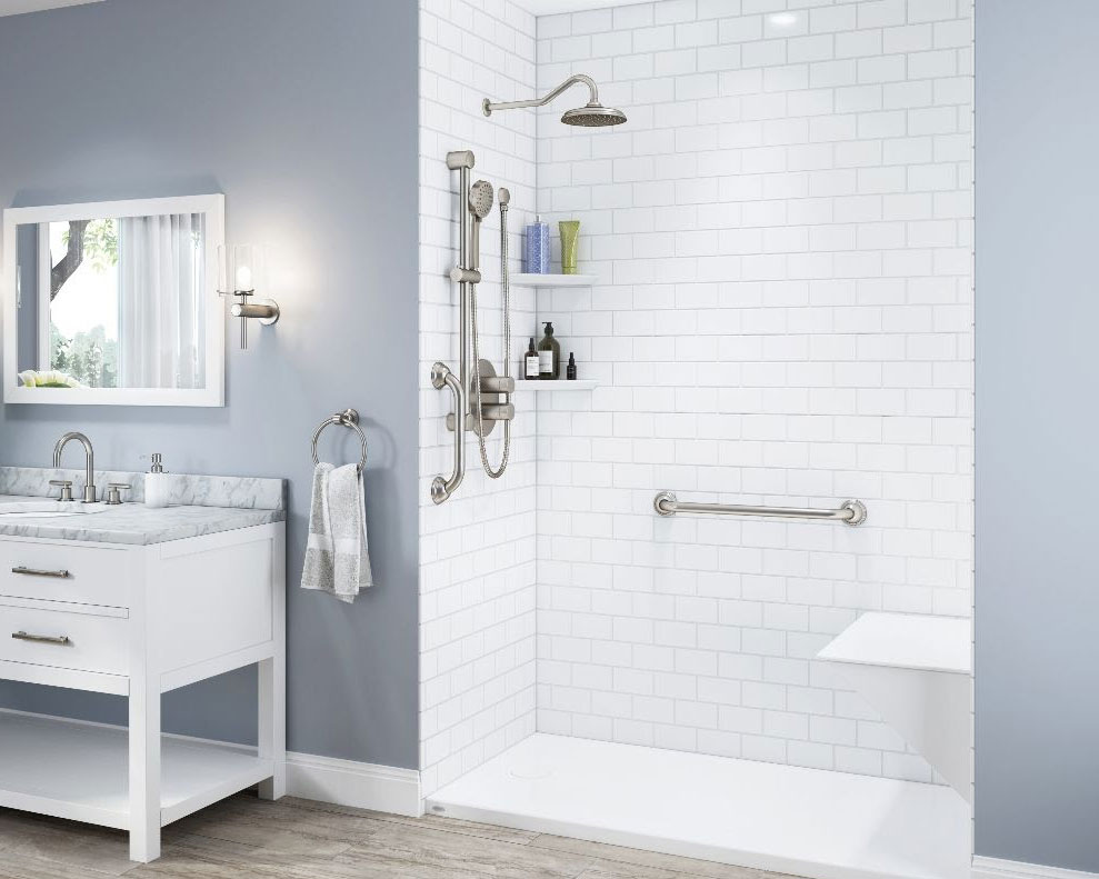 This image features a bright and airy bathroom with a walk-in shower area. The shower boasts a large rainfall showerhead and a separate handheld shower fixture, both with a stainless steel finish. The walls are lined with clean, white subway tiles and include built-in shelves holding various bath products. Safety features like a grab bar and a shower seat are present, indicating a design that caters to accessibility. To the left, there's a white vanity with a marble top and double faucets, above which hangs a rectangular mirror flanked by wall sconces. A towel ring next to the vanity holds a neatly hung towel. The floor is covered with light wood-look tiles, and a glimpse of the outdoors is seen through a window, contributing to the room’s serene and functional ambiance.