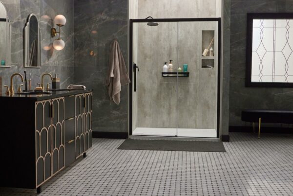 A modern bathroom with grey marble walls, a black vanity with gold accents, a glass-walled shower, hexagonal floor tiles, and stylish lighting fixtures.